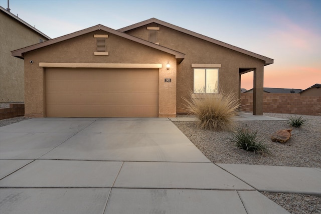 view of front of home with stucco siding, driveway, an attached garage, and fence