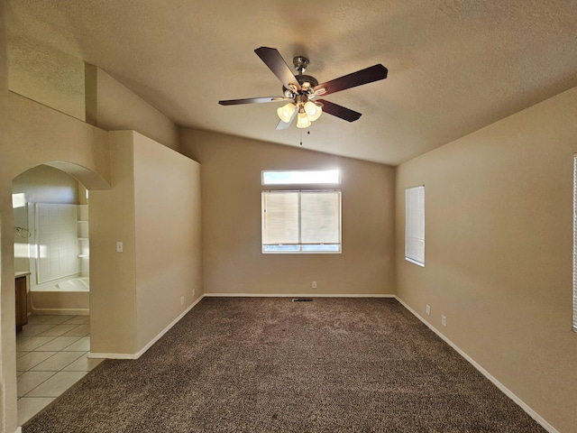 carpeted spare room with a ceiling fan, lofted ceiling, arched walkways, tile patterned flooring, and a textured ceiling