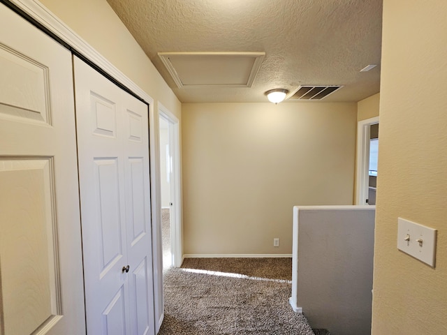 hallway with carpet, baseboards, visible vents, attic access, and a textured ceiling