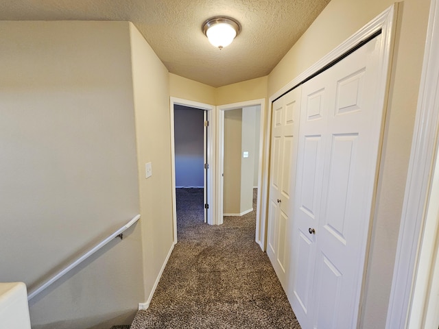 hallway featuring dark carpet, a textured ceiling, and baseboards