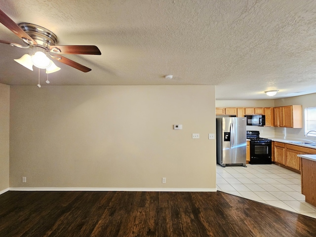 kitchen featuring baseboards, light wood-type flooring, light countertops, black appliances, and a sink