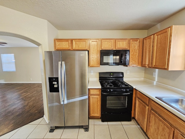 kitchen featuring black appliances, light tile patterned flooring, light countertops, and a sink