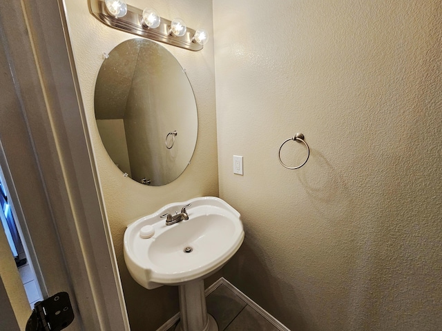 bathroom featuring tile patterned floors, a textured wall, baseboards, and a sink