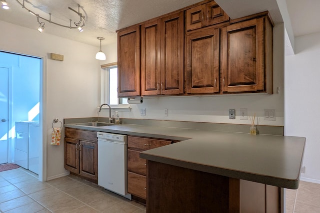 kitchen with a sink, washer and dryer, dark countertops, a peninsula, and white dishwasher