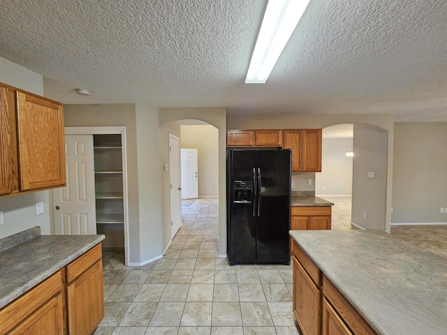 6619 Country Hills Ct NW, Albuquerque, NM 87114 - kitchen featuring arched walkways, black fridge with ice dispenser, brown cabinets, and a textured ceiling