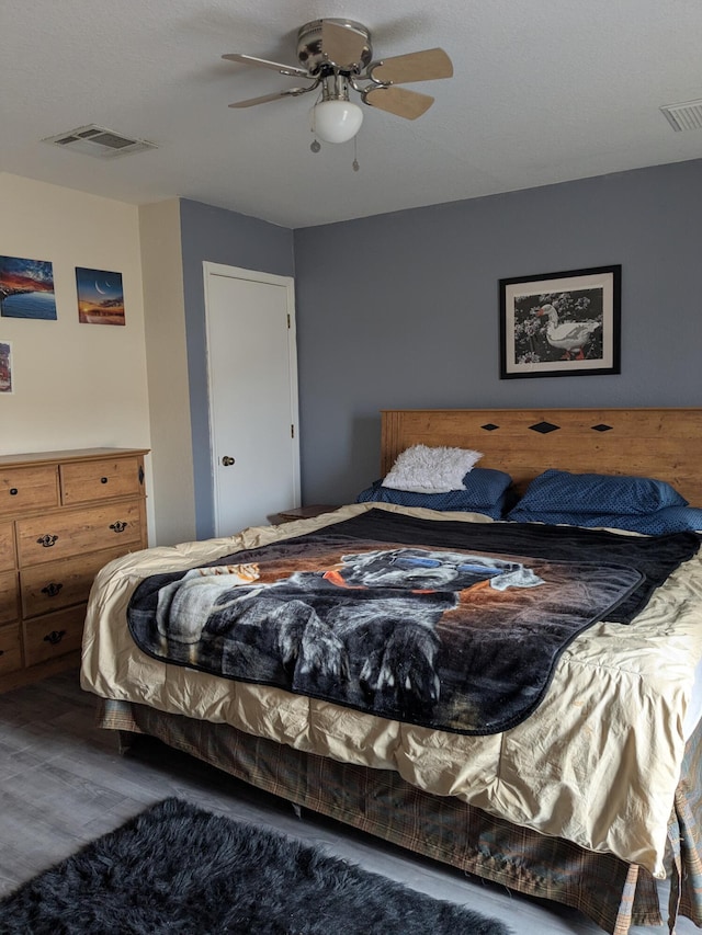 bedroom with ceiling fan, visible vents, and wood finished floors