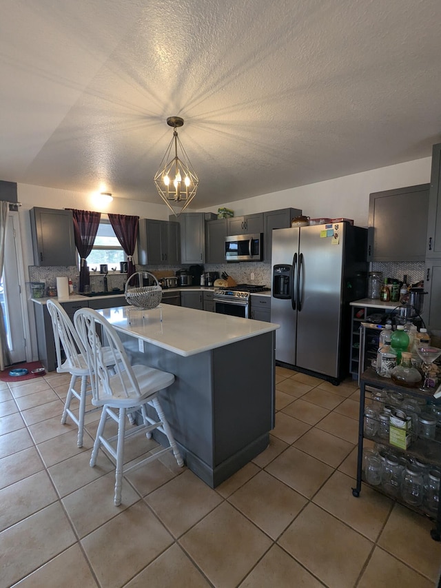 kitchen with light tile patterned flooring, stainless steel appliances, light countertops, backsplash, and a kitchen bar