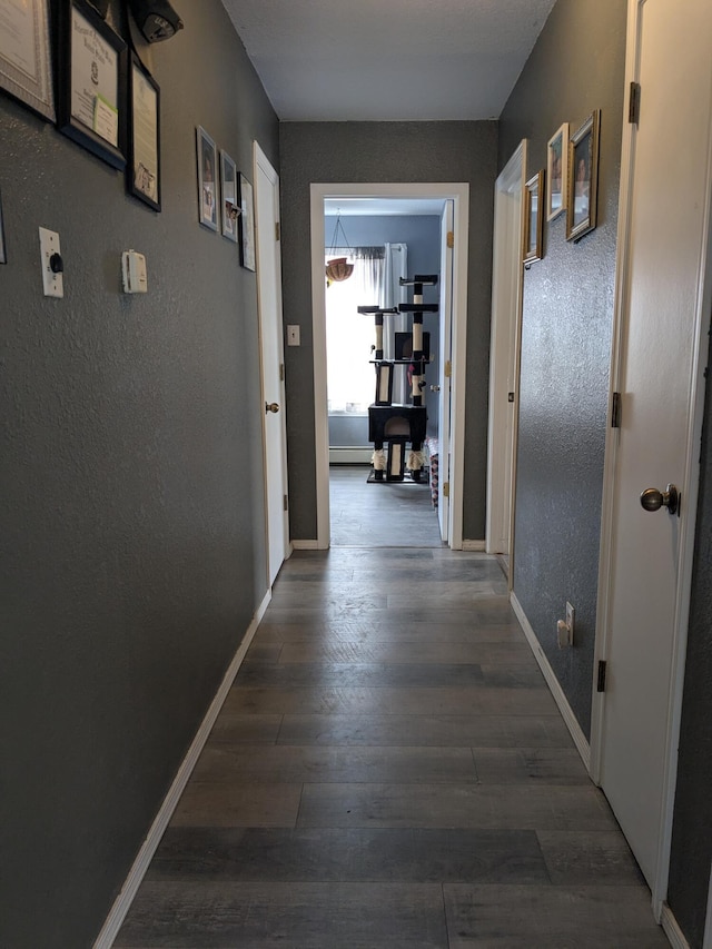 hallway featuring dark wood-style floors, baseboards, and a textured wall