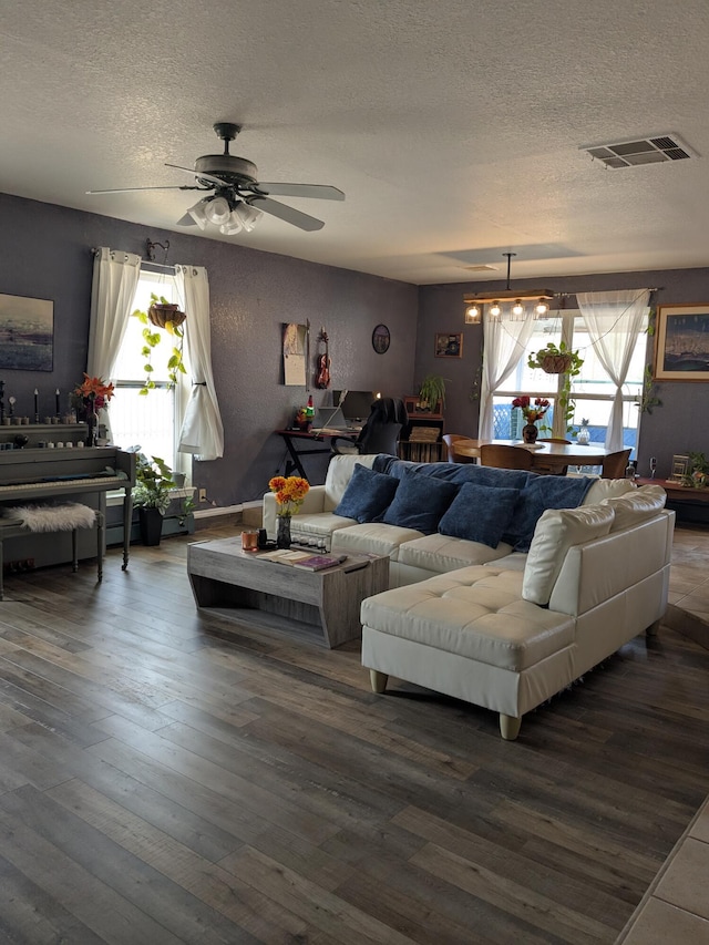 living room featuring a ceiling fan, a textured ceiling, visible vents, and wood finished floors