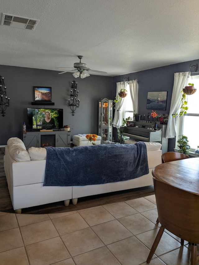 tiled living room featuring ceiling fan, visible vents, and a textured ceiling