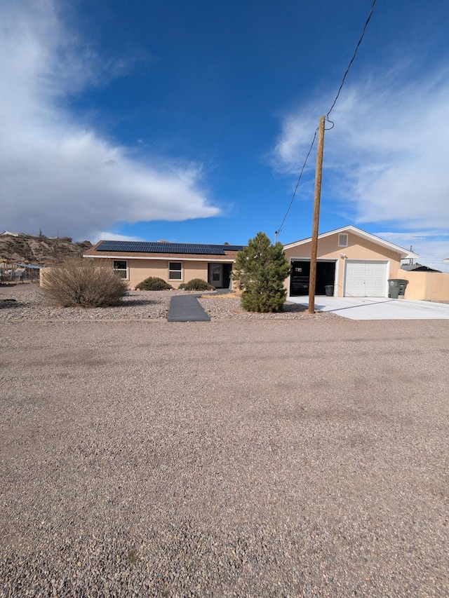 ranch-style house with roof mounted solar panels, a detached garage, and stucco siding