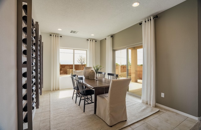 dining space featuring light tile patterned floors, baseboards, visible vents, and a textured ceiling