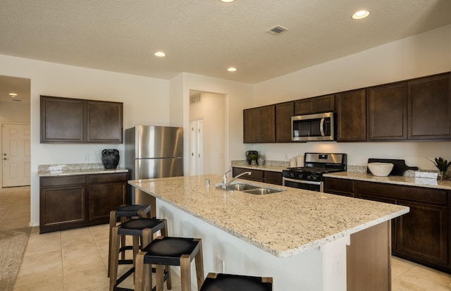 kitchen featuring dark brown cabinetry, visible vents, light stone counters, stainless steel appliances, and a sink