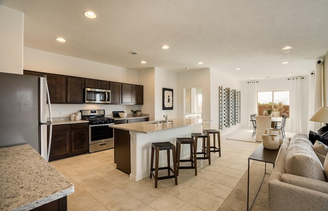 kitchen featuring dark brown cabinetry, stainless steel appliances, a breakfast bar, a sink, and open floor plan