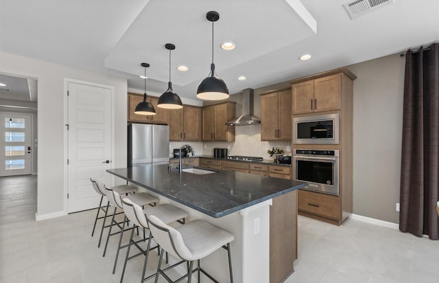 kitchen with visible vents, a sink, a kitchen breakfast bar, stainless steel appliances, and wall chimney range hood