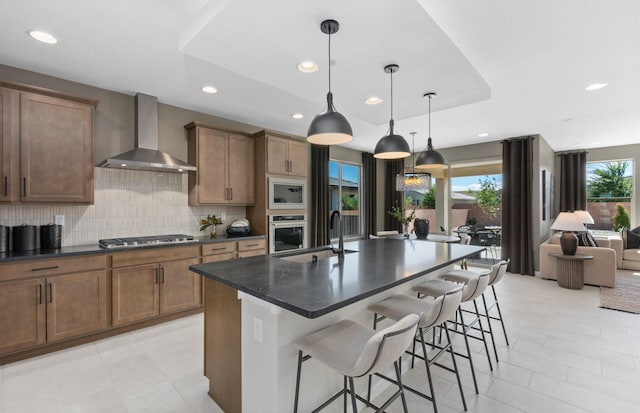 kitchen with wall chimney range hood, a breakfast bar, decorative backsplash, stainless steel appliances, and a sink