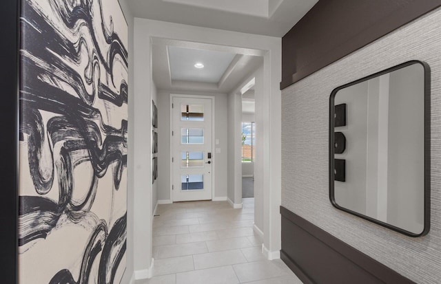 hall with a tray ceiling, light tile patterned floors, and baseboards