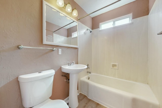 full bathroom with toilet, a textured wall, shower / bathtub combination, and a sink