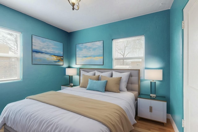 bedroom with multiple windows, baseboards, and wood finished floors