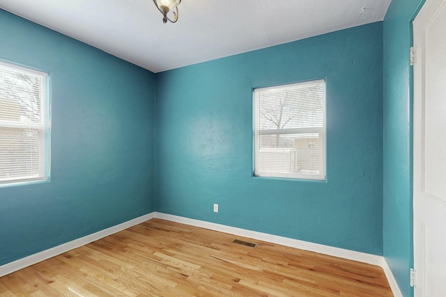 unfurnished room with visible vents, a healthy amount of sunlight, baseboards, and wood finished floors