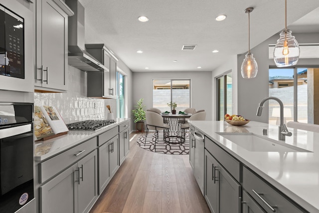 8401 Twain Way NW, Albuquerque, NM 87114 - kitchen with a sink, stainless steel appliances, wall chimney exhaust hood, gray cabinetry, and light wood-type flooring