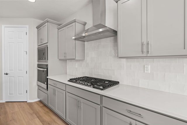 8401 Twain Way NW, Albuquerque, NM 87114 - kitchen with stainless steel appliances, wall chimney range hood, gray cabinets, light countertops, and light wood finished floors