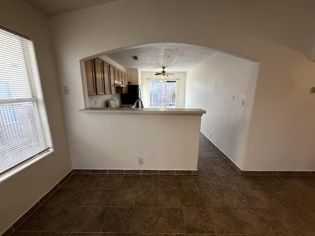 kitchen featuring light countertops, a peninsula, arched walkways, a textured ceiling, and a ceiling fan