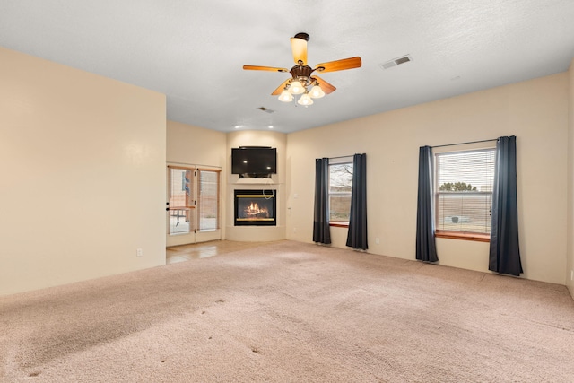 unfurnished living room with a glass covered fireplace, carpet flooring, visible vents, and ceiling fan