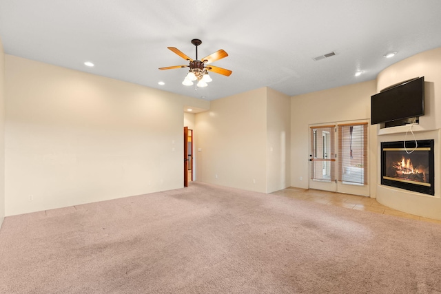 unfurnished living room with a glass covered fireplace, visible vents, a ceiling fan, and carpet