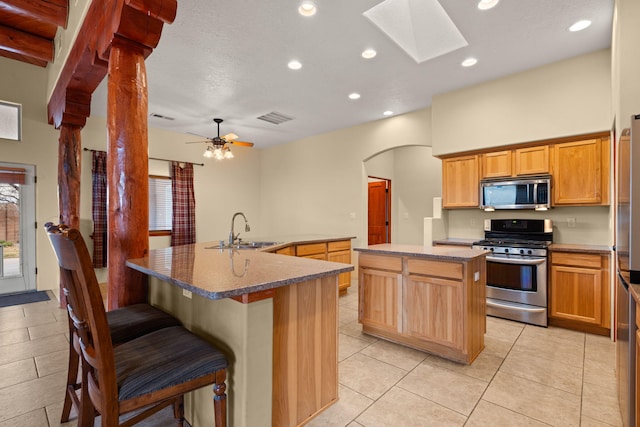 kitchen featuring a spacious island, visible vents, appliances with stainless steel finishes, arched walkways, and a sink