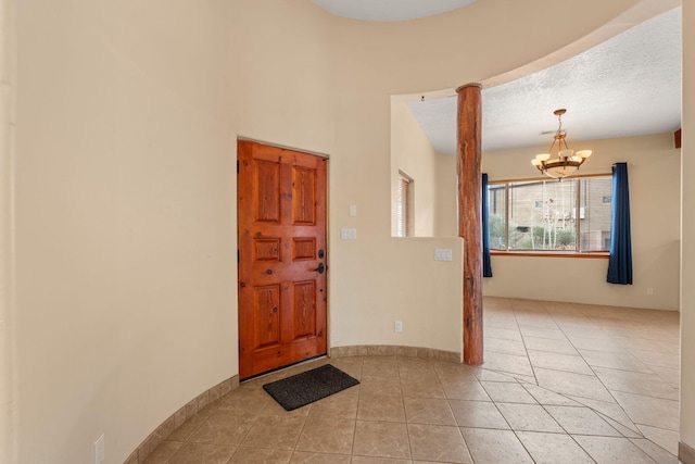 foyer entrance with light tile patterned floors, baseboards, a textured ceiling, and an inviting chandelier