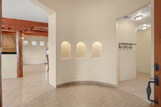 spare room with beamed ceiling, light tile patterned floors, and visible vents