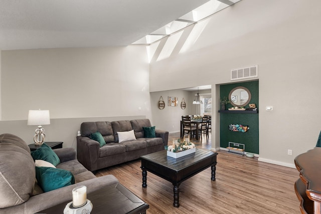 living room with wood finished floors, visible vents, baseboards, a skylight, and a towering ceiling