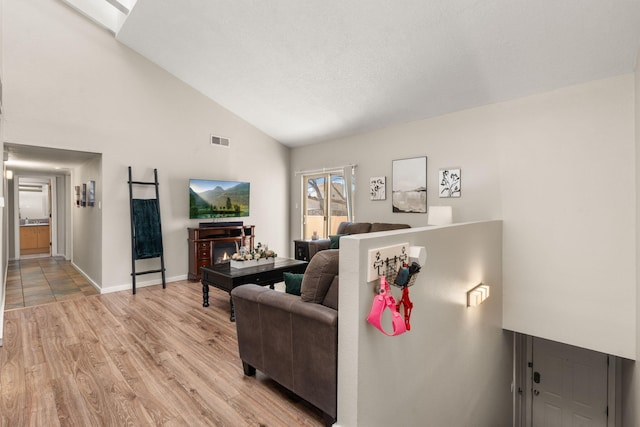 living area with high vaulted ceiling, light wood-style floors, visible vents, and baseboards