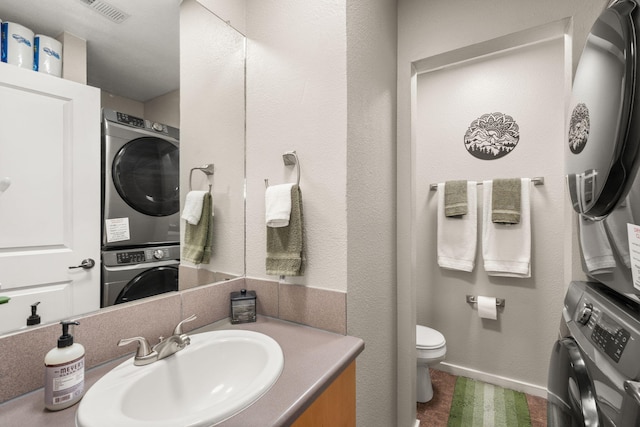 bathroom with vanity, visible vents, baseboards, stacked washer and clothes dryer, and toilet