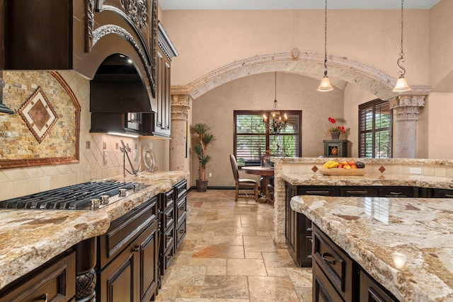 kitchen with stone tile floors, hanging light fixtures, arched walkways, and stainless steel gas stovetop