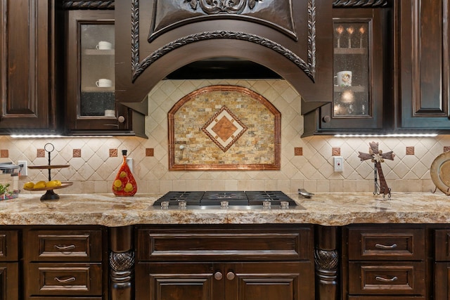 kitchen featuring dark brown cabinetry, stainless steel gas stovetop, glass insert cabinets, and custom range hood