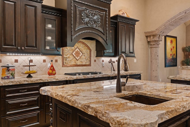 kitchen featuring stainless steel gas cooktop, premium range hood, light stone counters, and a sink