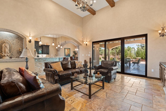 living area featuring a notable chandelier, stone tile floors, arched walkways, a high ceiling, and baseboards