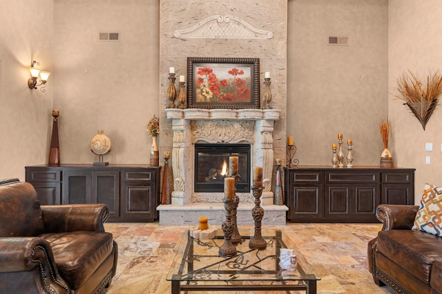 living area with stone finish flooring, visible vents, a towering ceiling, and a premium fireplace