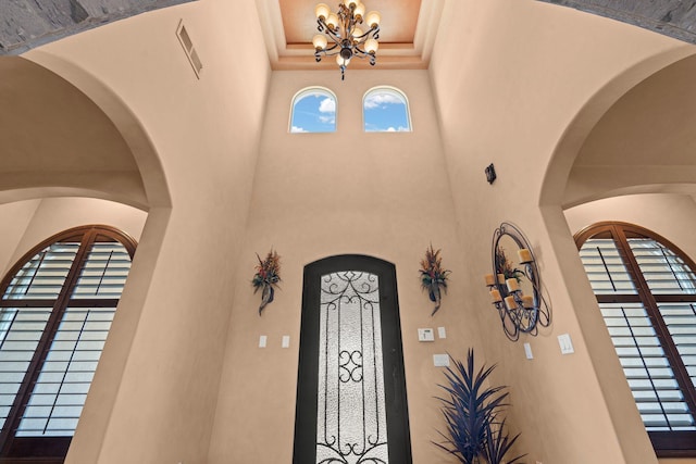 entryway featuring visible vents, a notable chandelier, crown molding, a raised ceiling, and a towering ceiling