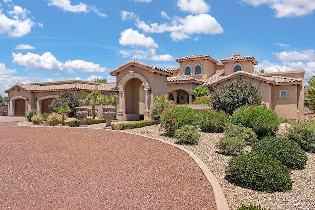 mediterranean / spanish house featuring a tiled roof, stucco siding, an attached garage, and driveway