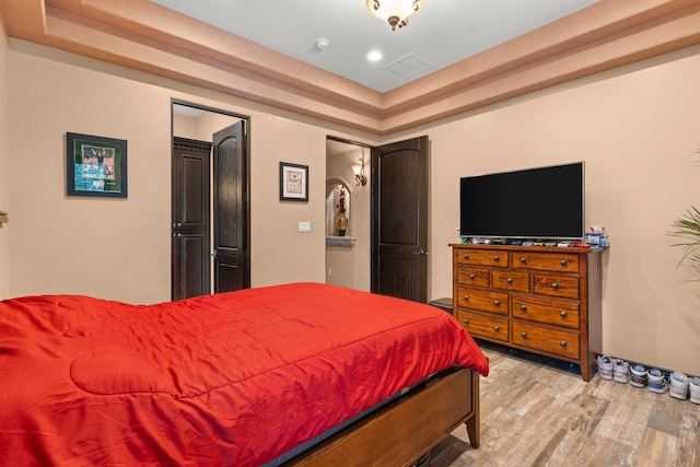 bedroom featuring visible vents, a tray ceiling, wood finished floors, recessed lighting, and baseboards