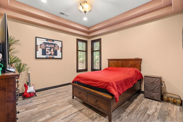 bedroom featuring a tray ceiling, wood finished floors, visible vents, and baseboards