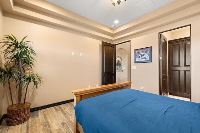 bedroom featuring visible vents, baseboards, light wood-type flooring, recessed lighting, and a raised ceiling