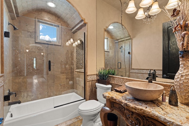 full bath featuring toilet, tile walls, bath / shower combo with glass door, vanity, and vaulted ceiling