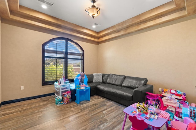 living room featuring visible vents, a raised ceiling, baseboards, and wood finished floors