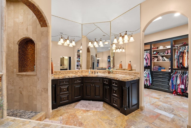 bathroom featuring a walk in closet, a walk in shower, vanity, and stone finish floor