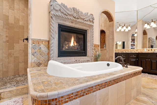 full bath featuring vanity, a glass covered fireplace, a tub, and tiled shower