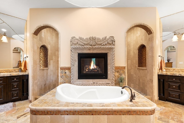 full bath featuring a bath, stone finish floor, a fireplace, and vanity